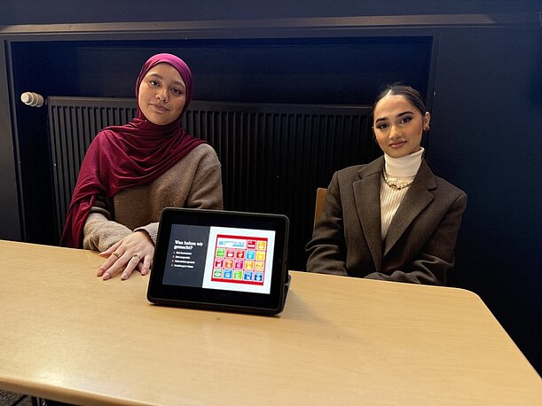 Zwei Schülerinnen präsentieren ein Tablet mit Projektergebnissen am Tisch