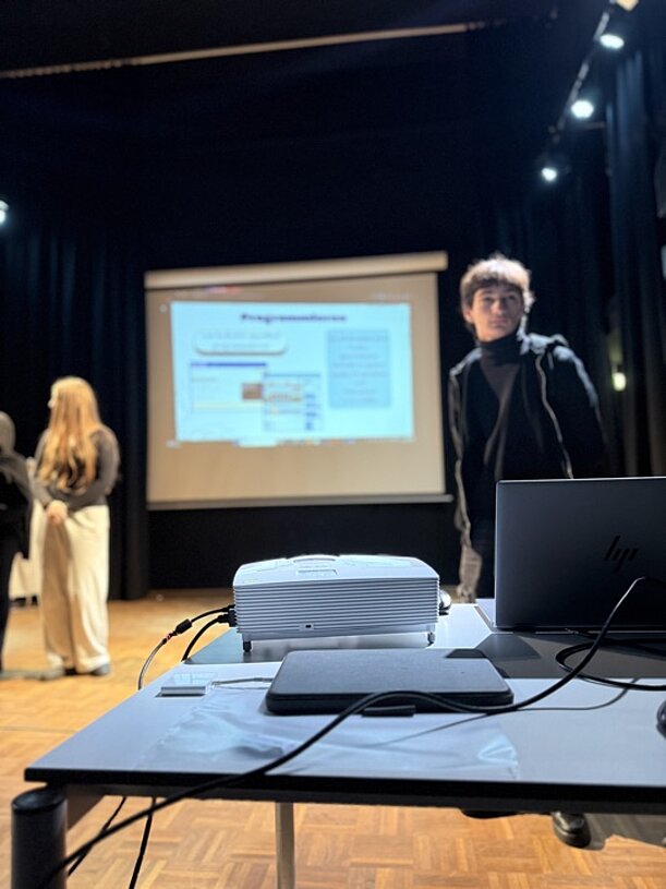 Beamer und Laptop vor Leinwand mit Präsentationsfolie auf der Bühne