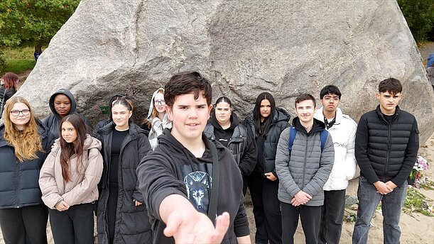 Gruppe Jugendlicher vor großem Felsbrocken, ein Schüler streckt die Hand aus