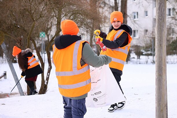 Kinder in Warnwesten sammeln Müll im verschneiten Park
