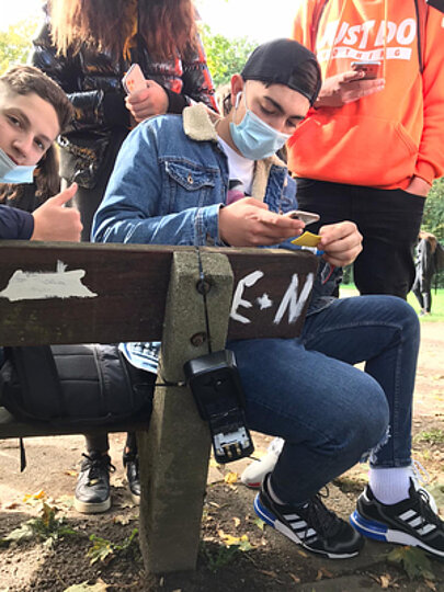 Schüler scannt auf einer Bank mit dem Smartphone einen Hinweis