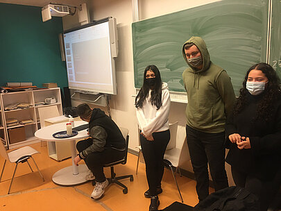 Schülerinnen und Schüler stehen im Klassenraum vor Tafel und Smartboard