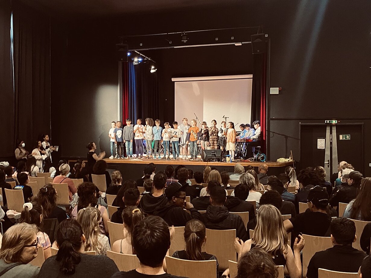 Voll besetzte Aula beim Musikfest mit Sängerinnen und Sängern auf der Bühne