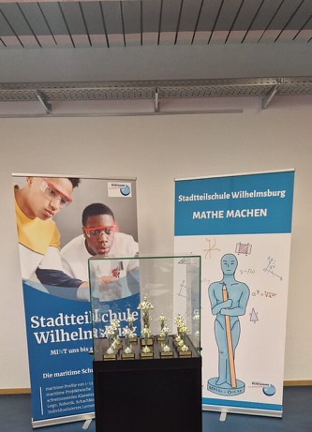 Mathe-Oscar-Pokale in einer Vitrine vor Aufstellern der Schule