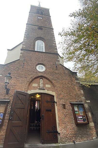 Backsteinkirche mit geöffneter Holztür im Amsterdamer Begijnhof