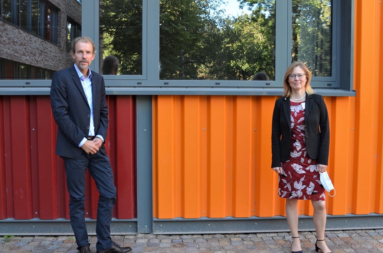 Landesschulrat und Frau vor bunter Fassade des Schulgebäudes