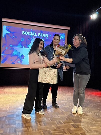 Schülerin erhält Blumen und Geschenk vor Leinwand „Social Star“