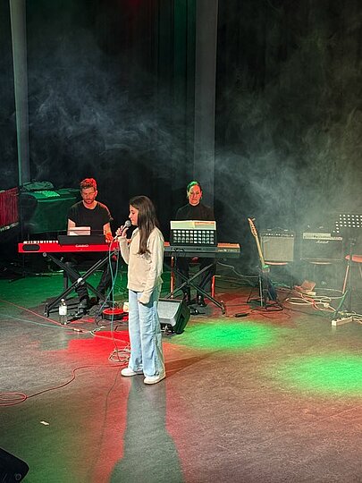 Sängerin mit Mikrofon vor Band im Bühnennebel beim Voice 2025