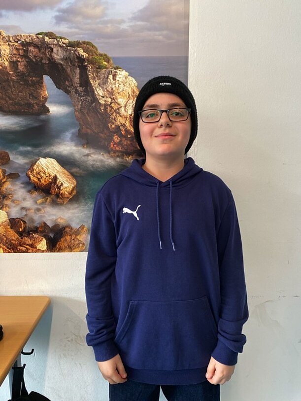 Emirhan aus der Klasse 6d steht vor einem Bild einer Felsküste