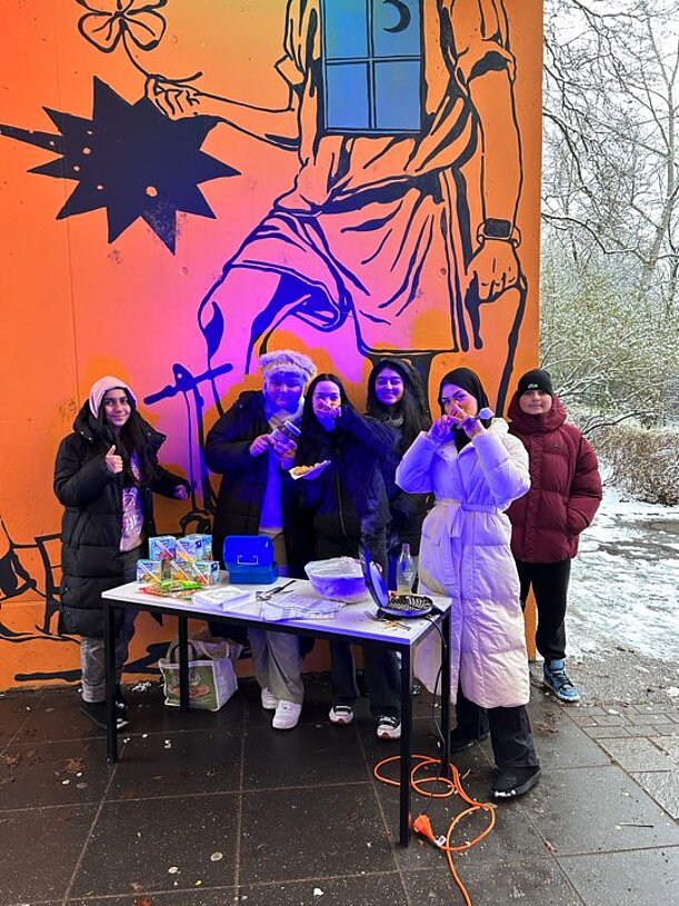 Jugendliche an einem Verkaufsstand vor bunt beleuchteter Wand im Schnee