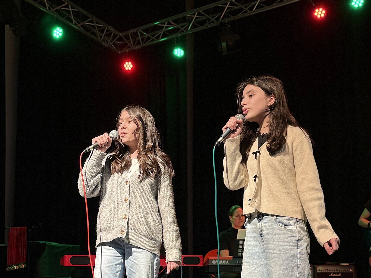 Rojbin und Melek aus der Klasse 5c singen auf der Bühne der Aula