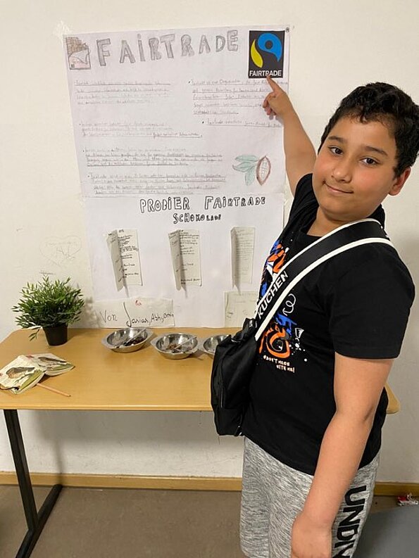 Abhinav Dass zeigt auf ein Fairtrade-Plakat mit Schokoladenproben