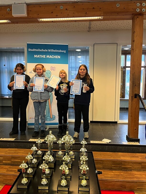 Vier Kinder mit Urkunden vor Pokalen beim MatheOscar