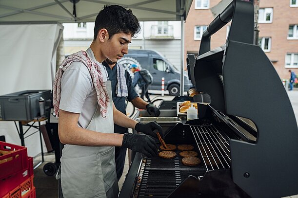Schüler grillt Burger-Patties am Grill beim Stadtteildinner