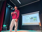 Schüler mit Mikrofon präsentiert sein Profilprojekt auf der Bühne vor einer Leinwand