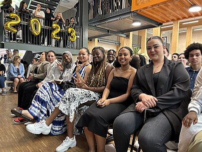 Absolventinnen sitzen in der ersten Reihe unter goldenen Ballonziffern 2023