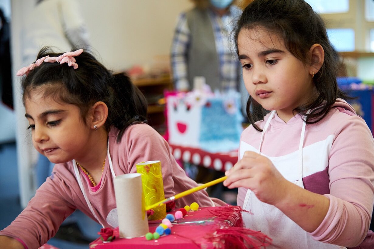 Zwei Vorschulkinder basteln an Masken aus Papprollen und Farbe