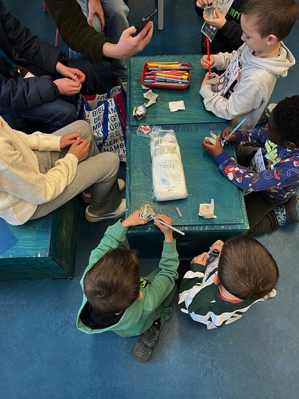 Kinder sitzen an einer Forscherstation mit Materialien
