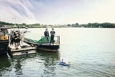 Modellboot fährt auf dem Spreehafen, Personen auf dem Ponton schauen zu