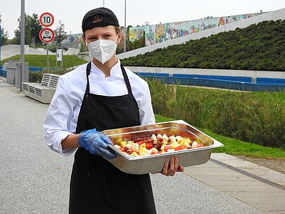 Jugendlicher in Kochkleidung hält Schale mit Obstsalat