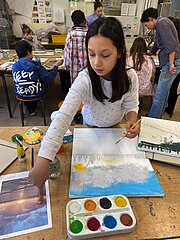 Hanna malt mit Wasserfarben ein Bild mit Wolken im Kunstprojekt