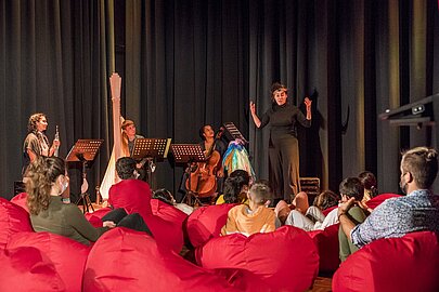 Musikerinnen spielen vor Kindern auf roten Sitzsäcken in der Aula