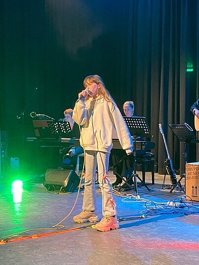 Sängerin in hellem Outfit bei grünem Bühnenlicht vor der Band