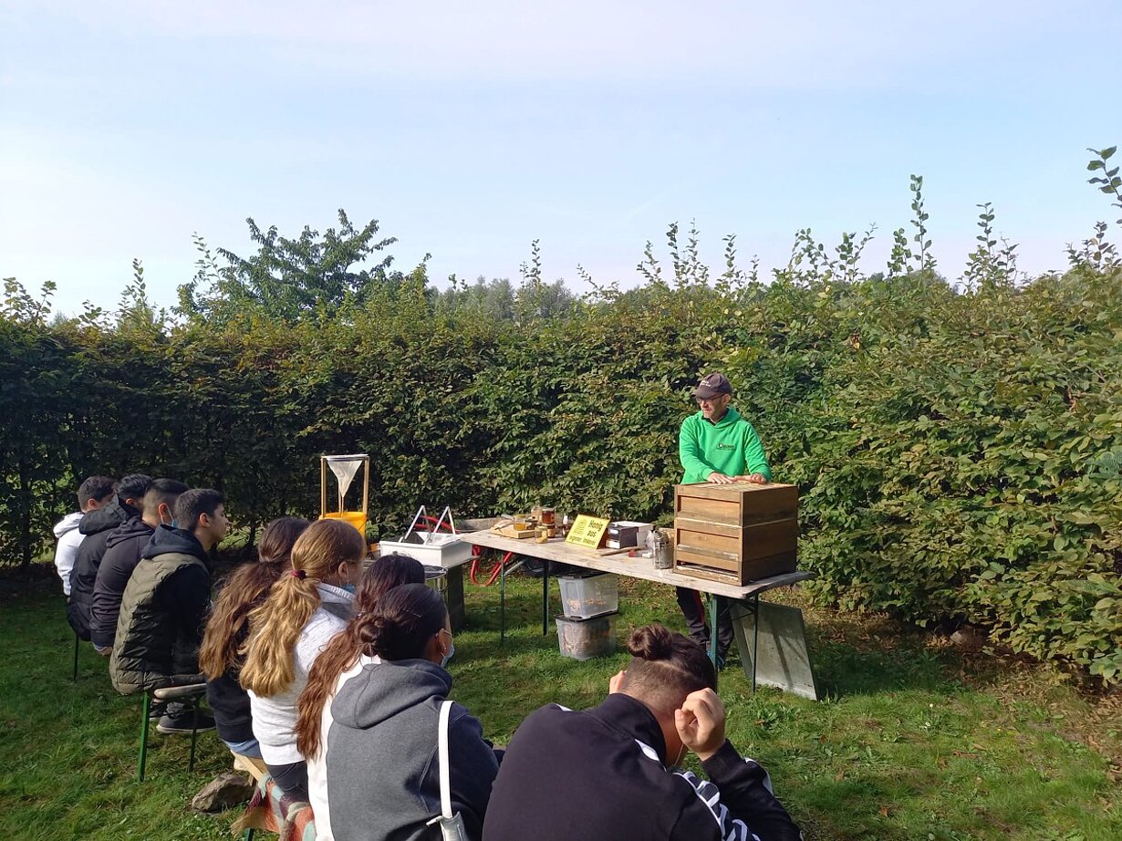 Imker erklärt Schülerinnen und Schülern im Garten die Bienenhaltung