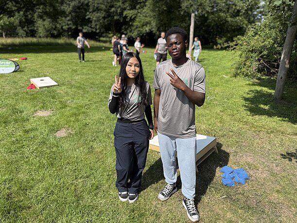 Zwei Jugendliche mit Peace-Zeichen beim Cornhole auf der Wiese