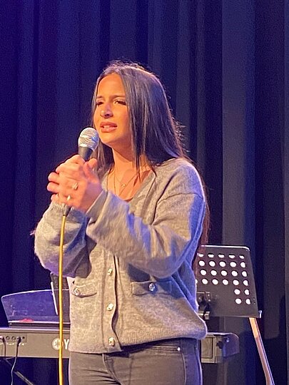 Sängerin in grauer Strickjacke singt mit Mikrofon