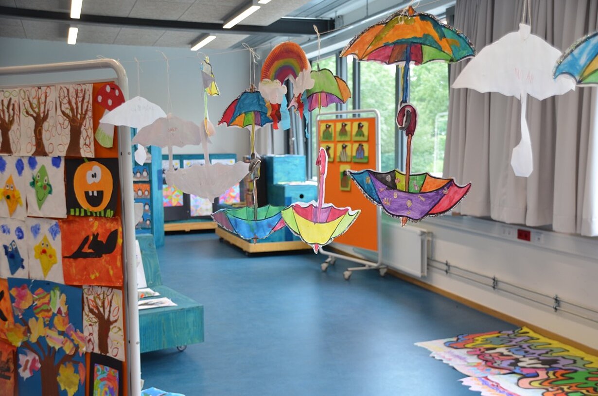 Ausstellungsraum mit bemalten Schirmen und Kinderbildern der Vorschule