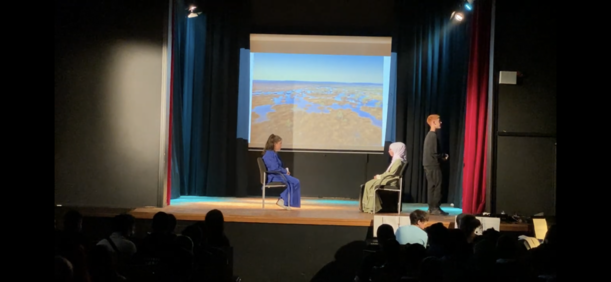 Klasse 8d spielt Szene mit zwei Sitzenden vor projizierter Landschaft