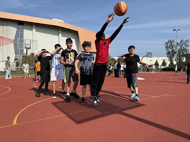 Jugendliche spielen Basketball auf einem roten Platz im Inselpark