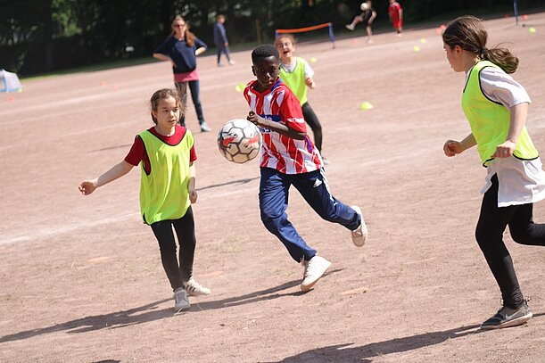 Kinder spielen Fußball auf einem Sandplatz beim Sporttag