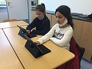 Zwei Grundschülerinnen arbeiten am Tisch mit Leih-Tablets