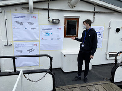 Schüler präsentiert Plakate an der Wand im Inneren eines Schiffes