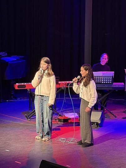 Zwei Schülerinnen singen gemeinsam, im Hintergrund Keyboardbegleitung