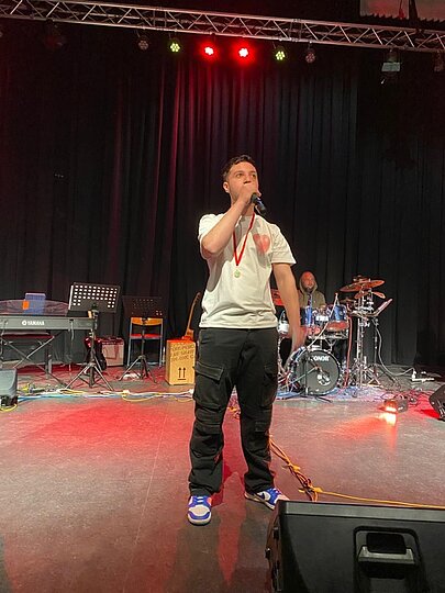 Sänger in weißem T-Shirt mit Band im Hintergrund