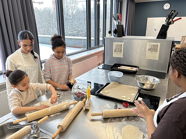 Kinder rollen Teig mit Nudelhölzern in der Schulküche am Tag der offenen Tür