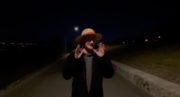 Standbild aus einem Schulvideo: Person mit Hut gestikuliert nachts im Freien