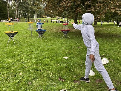 Schüler wirft Frisbee auf Discgolf-Körbe im Park