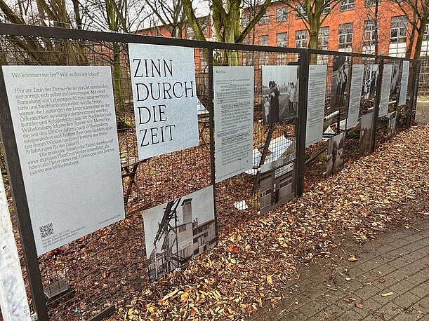 Ausstellungstafeln „Zinn durch die Zeit“ am Zaun vor den Zinnwerken