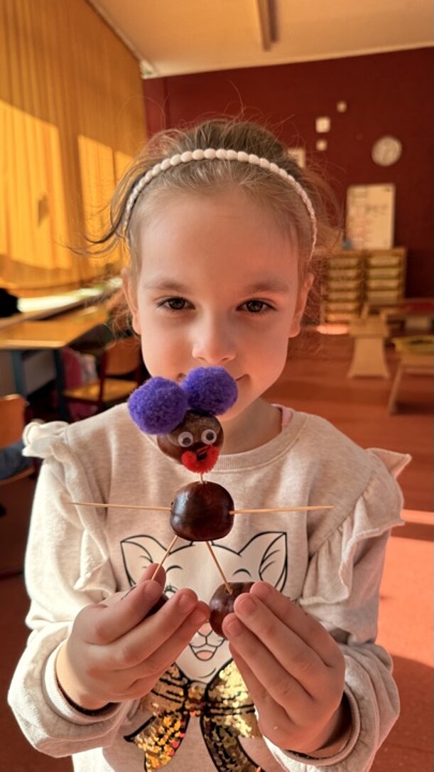 Mädchen hält Kastanienfigur mit lila Pompon-Haaren